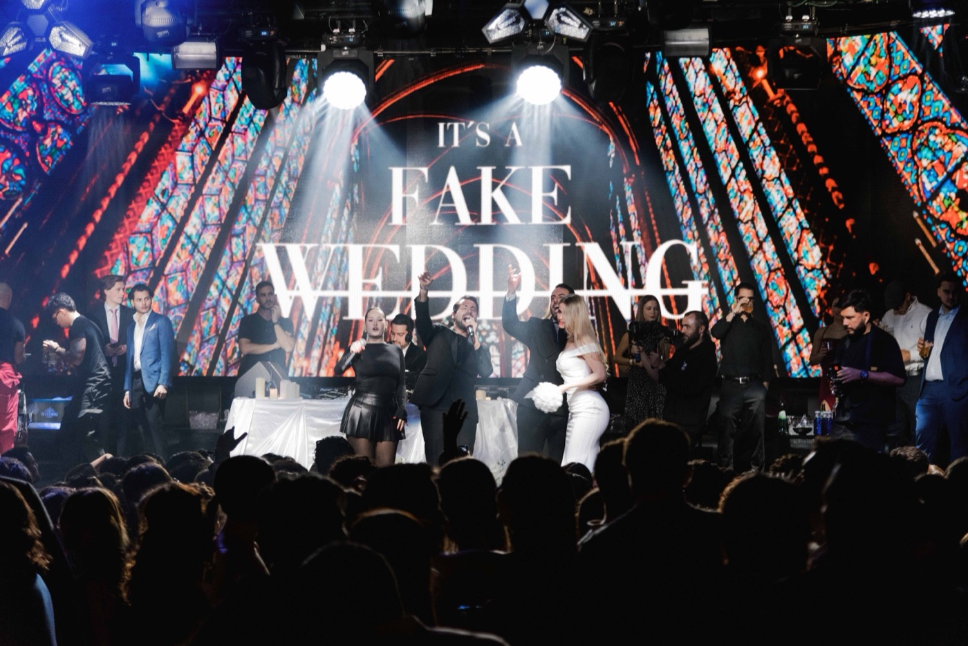 Live performers on the It's a Fake Wedding stage under the stained-glass screen